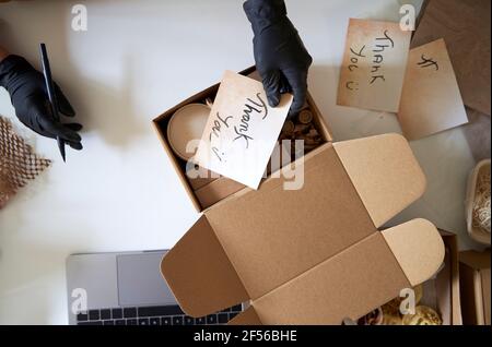 Le mani della donna che mettono l'etichetta di ringraziamento nella scatola all'officina Foto Stock