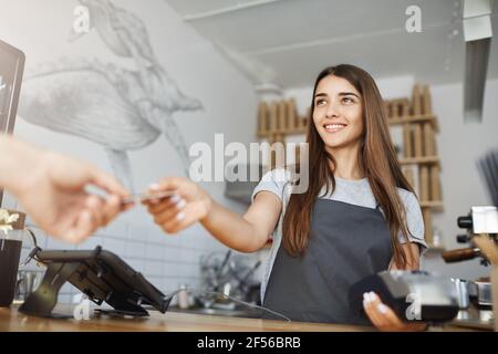 Barista femminile che interagisce con il cliente utilizzando un terminale bancario per elaborare e acquisire pagamenti con carta di credito. Foto Stock