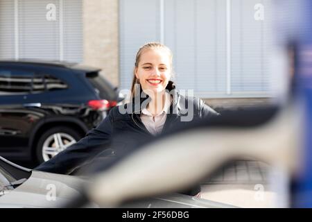 Ritratto di giovane bella bionda in piedi all'aperto e sorridente a. fotocamera Foto Stock
