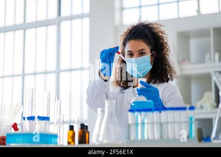 Giovane dottoressa che esamina la soluzione chimica in laboratorio durante COVID-19 Foto Stock