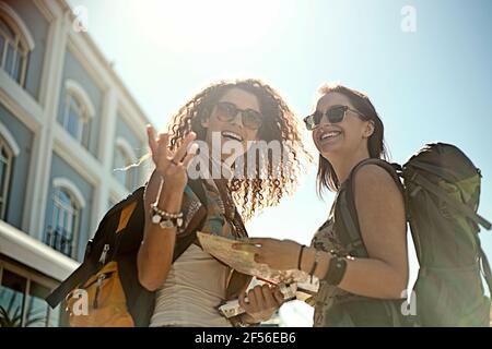 Allegre amiche che discutono sulla mappa mentre gesturano contro il cielo il giorno di sole Foto Stock
