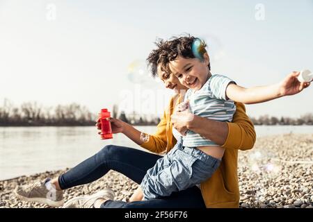 La mamma e il figlio giocosi giocano con il sapone di bolla sul sole giorno Foto Stock