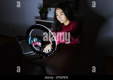 Giovane donna cinese vlogger seduta con computer portatile e anello illuminato leggero Foto Stock