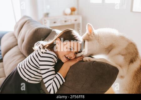 Ragazza sorridente appoggiata sul divano con Husky siberiano a casa Foto Stock