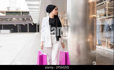 Donna araba premurosa che indossa un copricapo che tiene le borse mentre lo shopping a. centro commerciale Foto Stock