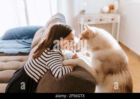 Ragazza sorridente con gli occhi chiusi appoggiandosi su un divano con siberiano Husky a casa Foto Stock