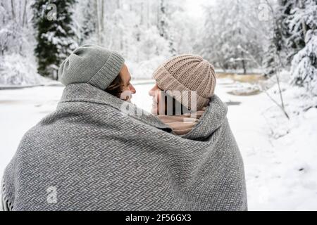 Coppia sorridente coperta di coperta seduta dal fiume congelato dentro foresta Foto Stock