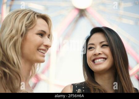 Sorridendo le amiche contro la ruota panoramica al parco divertimenti Foto Stock