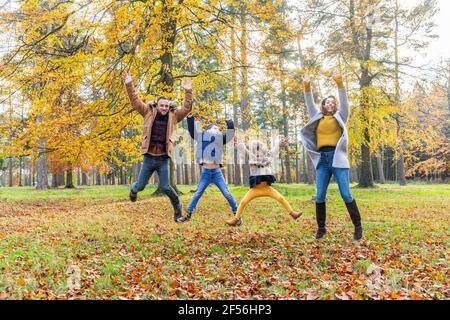 Famiglia giocosa con le mani sollevate saltando insieme nella foresta Foto Stock