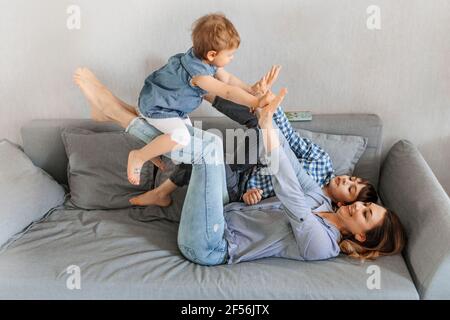 Madre che solleva la figlia da un figlio sul divano a casa Foto Stock