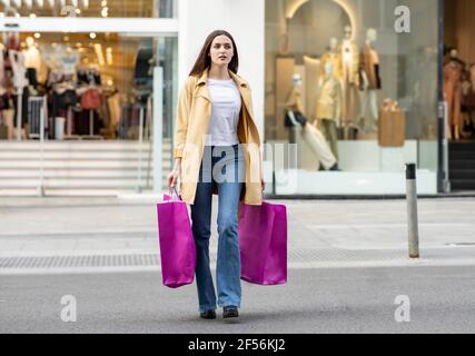 Giovane donna che cammina con borse di shopping color magenta di fronte del negozio Foto Stock