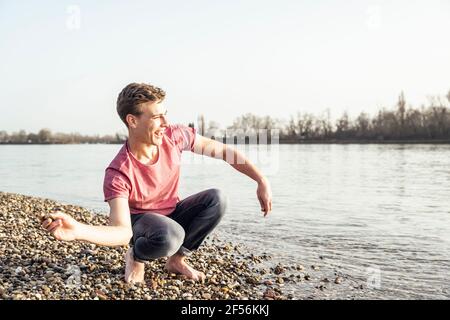 Giovane uomo allegro gettando ciottoli in lago il giorno di sole Foto Stock