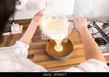 Donna che versa il ripieno di cheesecake sulla pasta di biscotti sbriciolati Foto Stock