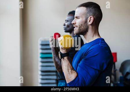 Atleti maschili che si allenano con i manubri durante l'allenamento sportivo in palestra Foto Stock