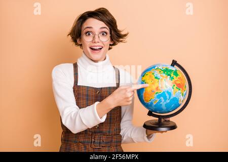 Ritratto fotografico del nerd femminile intelligente eccitato che punta il dito globo in vetri isolati su sfondo di colore beige pastello Foto Stock