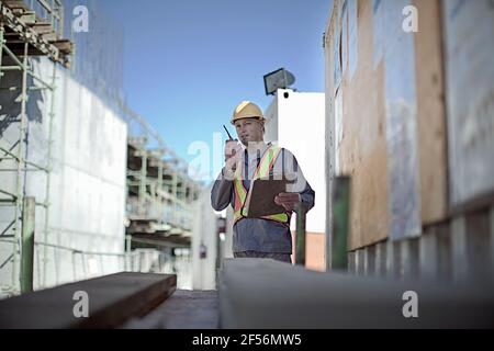 Lavoratore di costruzione maschile che parla su walkie-talkie in cantiere Foto Stock