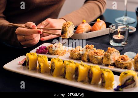 Un giovane cliente che mangia sushi con le bacchette al ristorante Foto Stock