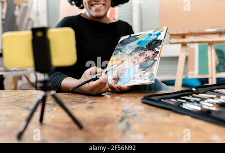 Giovane artista femminile che mostra la tavolozza di vernice mentre vlogging attraverso Smart telefono in studio Foto Stock