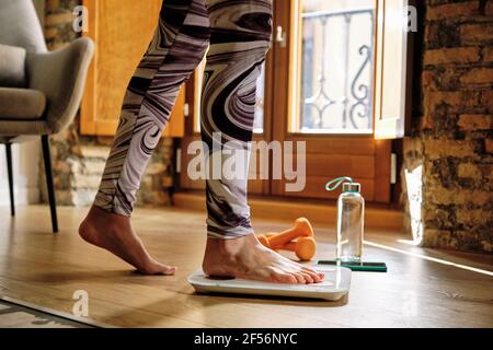 Donna che controlla il peso mentre si sta sulla bilancia a casa Foto Stock