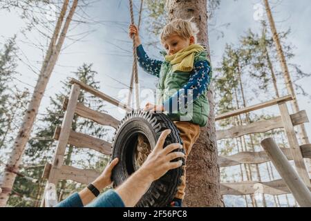 Uomo che tiene la fila mentre il figlio pende attraverso la corda contro l'albero a Salzburger Land, Austria Foto Stock