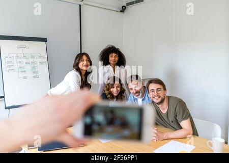 Uomo che fotografa uomini e donne imprenditori attraverso smartphone in sala riunioni in ufficio Foto Stock
