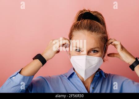 Donna d'affari che indossa una maschera protettiva FFP2 mentre si sta in piedi contro colorato sfondo Foto Stock