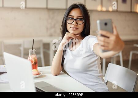 Donne come se stesse. Giovane studente asiatico che fa un selfie al caffè utilizzando un telefono cellulare che sembra abbastanza impressionante. Foto Stock