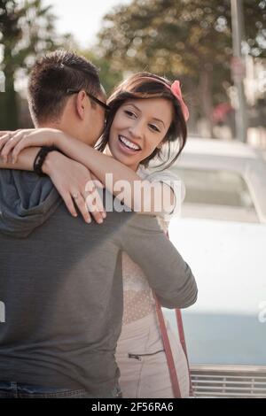 Ragazza sorridente che abbracciava il ragazzo in piedi contro l'auto Foto Stock