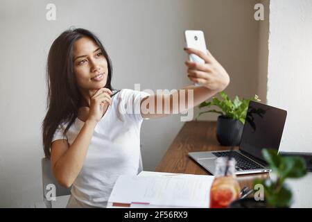 Giovane studente che fa un selfie in caffetteria durante la pausa estiva facendo divertimento di se stessa lavorando al laptop sognando del suo proprio commercio in linea. Foto Stock