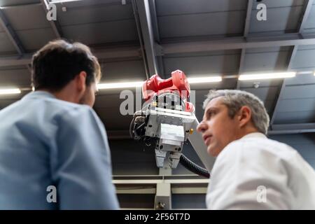 Ingegneri maschi che discutono al braccio robotico in fabbrica Foto Stock