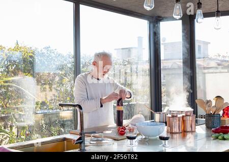 Uomo anziano che lavora mentre si trova in cucina a casa Foto Stock