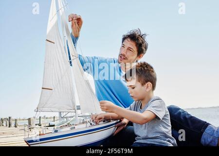 Padre e figlio preparano insieme il giocattolo a vela mentre si siedono molo Foto Stock