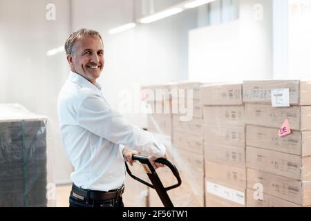 Sorridente uomo d'affari senior che tiene il pallet jack in magazzino Foto Stock