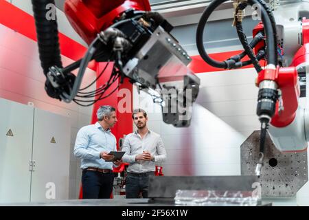 Gli ingegneri di automazione maschili discutono mentre i macchinari robotici sono in primo piano Foto Stock