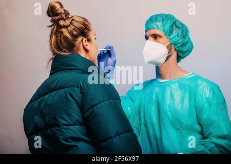 Esperienza maschile che prende il test medico COVID-19 del paziente mentre si è in piedi contro sfondo grigio Foto Stock
