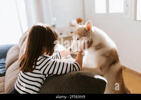 Ragazza che accarezzava Husky siberiano mentre si appoggiava sul divano a casa Foto Stock
