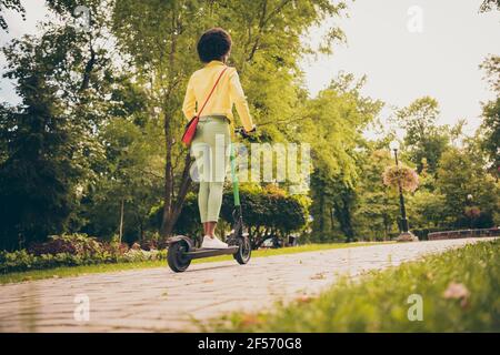 Posteriore dietro la vista a tutta lunghezza del corpo di lei lei bella sportiva snella fit sottile capelli ondulati ragazza godendo di guida scooter elettrico che passa soleggiato Foto Stock