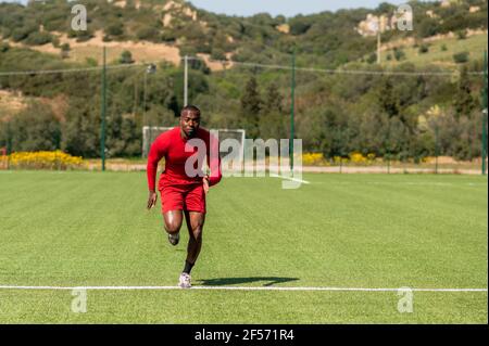 Sportivo africano grandangolare che corre veloce in un campo di calcio. Foto Stock