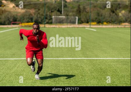 Corridore professionale nero afro che corre veloce in un campo con il viso concentrato serio. Spazio di copia a destra. Foto Stock