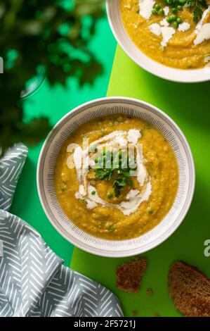 Zuppa vegetariana di crema di zucca guarnita con piselli verdi freschi e foglie di prezzemolo su sfondo verde vibrante Foto Stock