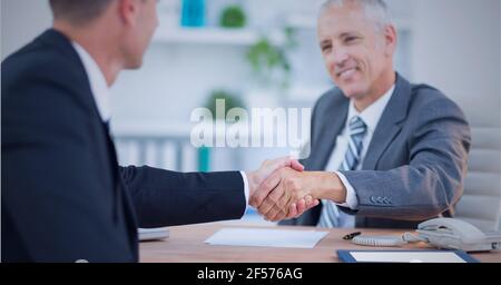 Uomini d'affari sorridenti che scuotono le mani sulla scrivania in ufficio Foto Stock