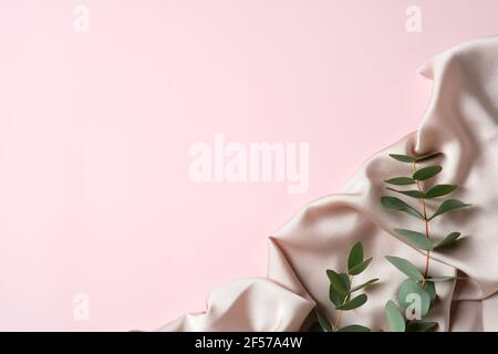 Composizione piatta con tessuto e foglie di eucalipto su fondo rosa. Modello di biglietto di auguri per il giorno della mamma. Foto Stock