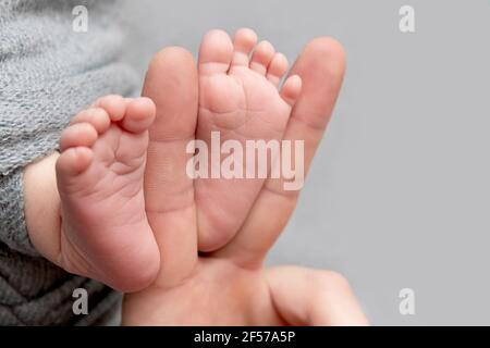 Il padre tiene i piedi del neonato. Colore grigio. Tenerezza. Concetto del giorno del Padre. Foto Stock