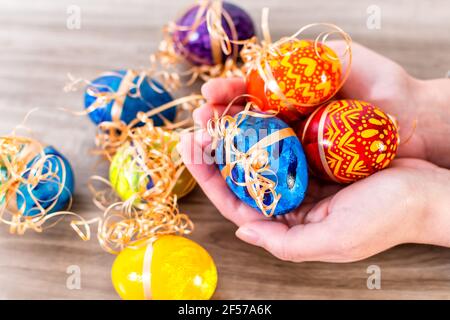 Colpo di primo piano di una mano di donna che tiene decorate uova di pasqua su sfondo di legno Foto Stock