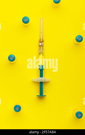 Siringa con diversi flaconcini medici per l'iniezione su sfondo giallo. Vista dall'alto. Foto Stock