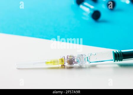 Primo piano della siringa con diversi flaconcini medici dietro su sfondo bianco e blu. Foto Stock