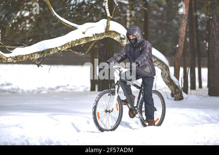 Sport invernali. Escursioni in bicicletta. Un giovane in abiti neri guida una bicicletta. Foto Stock