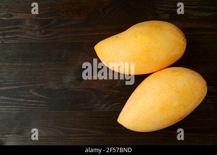 Vista dall'alto di due frutti di mango freschi e maturi isolati Sfondo di legno nero Foto Stock