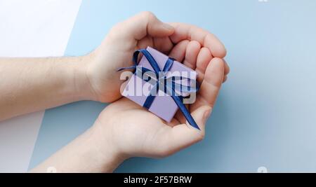 Confezione regalo viola con prua blu in mani maschili su sfondo azzurro. Vista dall'alto. Spazio di copia. Foto Stock