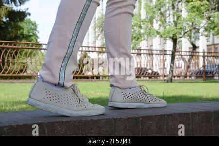 Le gambe di una ragazza in sneaker bianche e pantaloni rosa. Vista laterale. Un adolescente in pantofole bianche nella città.UNA giovane donna in scarpe atletiche sta camminando. S Foto Stock